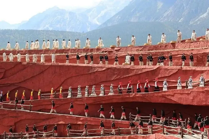 Große Gruppe von Darstellern in traditioneller Kleidung auf terrassierten roten Bühnen im Freien.