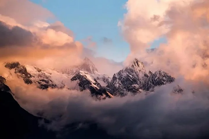Schneebedeckte Berggipfel ragen bei Sonnenuntergang oder Sonnenaufgang über dichte Wolken.
