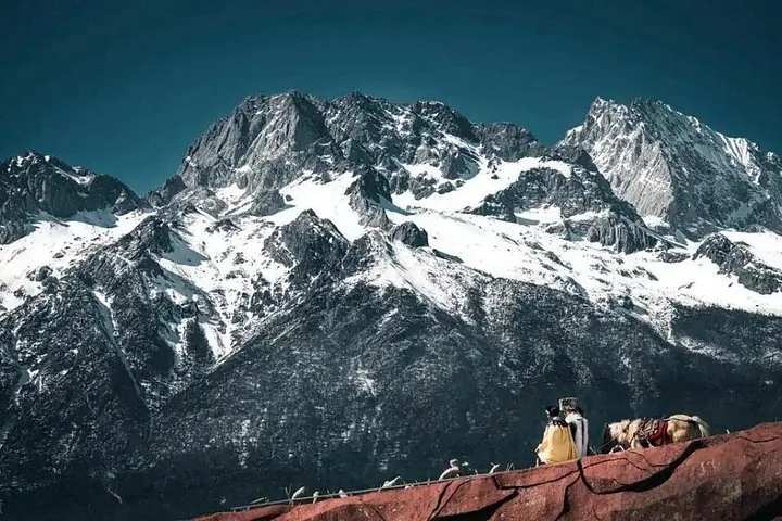 Menschen auf einer roten Felsformation betrachten gewaltige schneebedeckte Berggipfel.