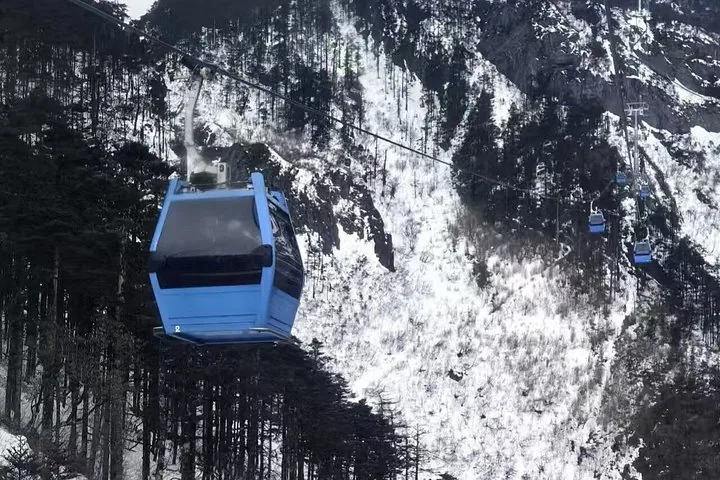Blaue Seilbahn fährt über eine verschneite, bewaldete Berglandschaft.